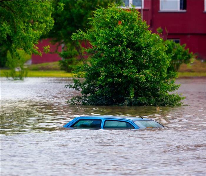 Image of a flooded street causing damage to a car and homes
